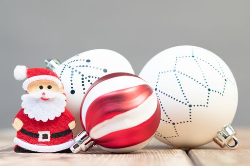 A closeup shot of a small wooden Santa Claus figurine with ball ornaments on the table under the lights