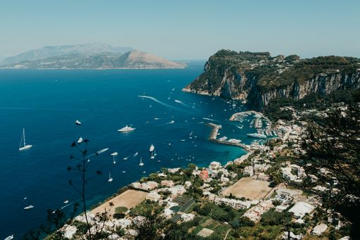 A view of a body of water near the beach with sailing ships and rocky mounatins