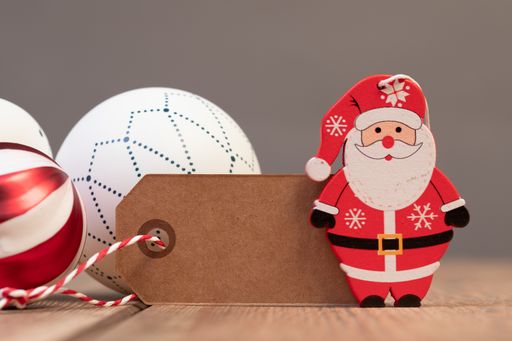 A closeup of a small wooden Santa Claus figurine with Christmas ball ornaments and a blank wish tag on the table