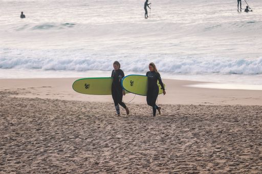 Two women surfers walking on the beach holding surfboards