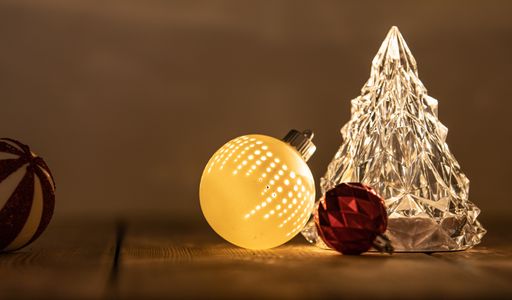 A closeup shot of ball ornaments and a glass Christmas tree on the table under the lights