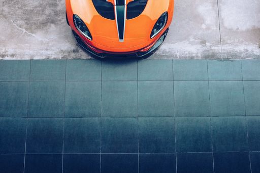 A top view of the front part of a modern orange car parked near a floor with dark grey tiles