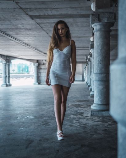 An attractive young female with long hair and white dress posing for the camera near columns