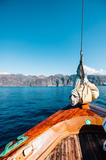 A vertical shot of a seascape in the background of cliffs from the wooden boat.