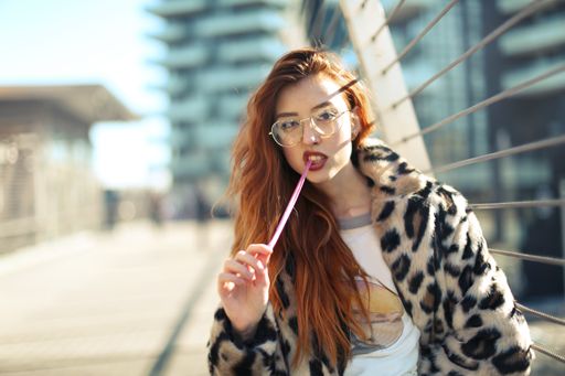 An attractive young female with glasses wearing a coat and chewing a gum