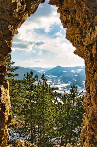 A beautiful landscape view from a stone cave to aerial wood trees, ice glacier and a gray cloudy sky