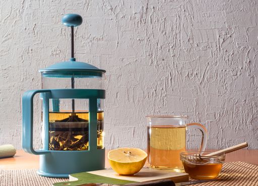 A herbal tea in a teapot next to a cup, lemon and honey.