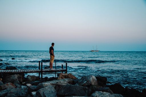 A side view of the young man on the pier over the wavy sea water at sunset