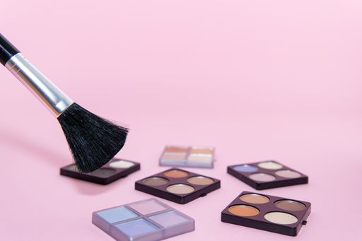 Make-up set with various colors and a brush on pink background. Beauty concept, copy space