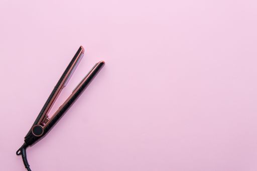 Top view of black hair straightening iron on pink background. Hair care concept, copy space