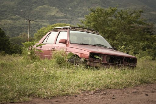 A front view of an old damaged broken red car parked in nature