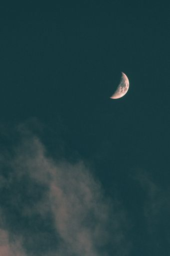 A vertical low angle shot of the moon above the clouds in the blue sky