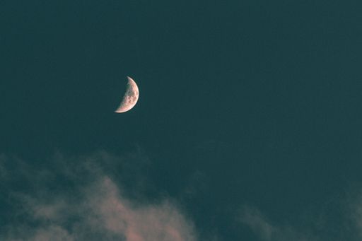 A low angle shot of the moon above the clouds in the blue sky