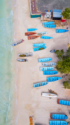 An aerial shot of blue boats moored on the sandy shore