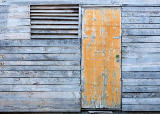 A yellow old door and a window with a wooden gate on the facade of a barn