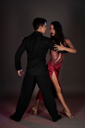 A vertical shot of a Hispanic woman and an East Asian man dancing passionate tango on a studio background.