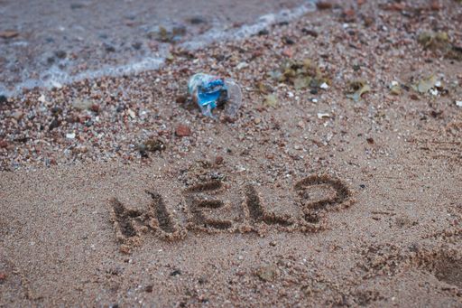 A help message written on the beach next to plastic waste.