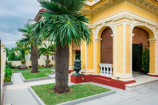 A partial view of a classic home on a tropical place with palm tress garden on a cloudy day.