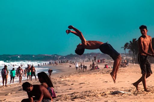 A Caucasian  young man doing a head flip at the beach feeling strong