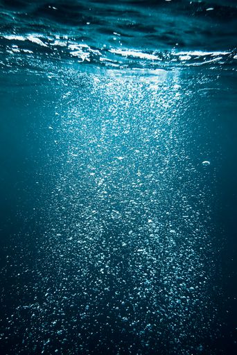 A vertical shot of air bubbles rising up under water and sunlight penetrating from the above
