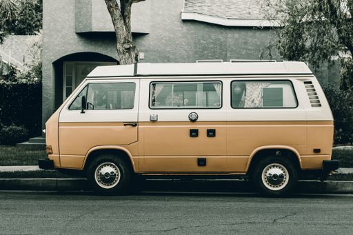 A closeup shot of a small white and orange van parked on the road near a house