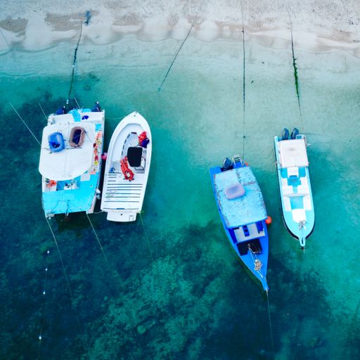 A vertical shot of four boats parked near a shore of a bright blue sea