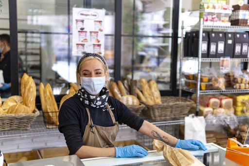 A young female in a face mask and plastic gloves working in the bakery during the COVID-19 pandemic