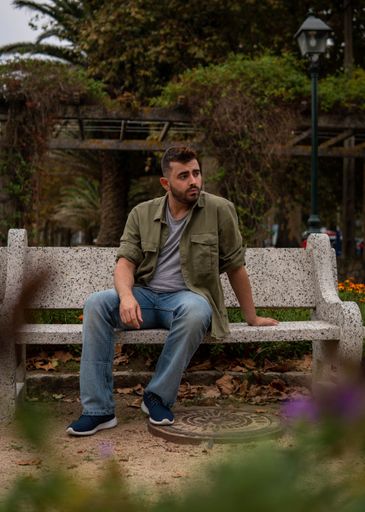 A vertical shot of Caucasian 24 years old male on the beach in Spain sitting on a park bench