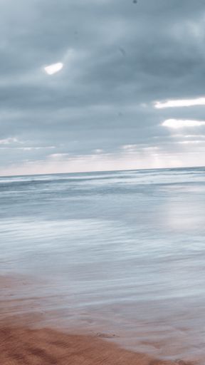 A vertical shot of a seascape reflecting the cloudy skies above