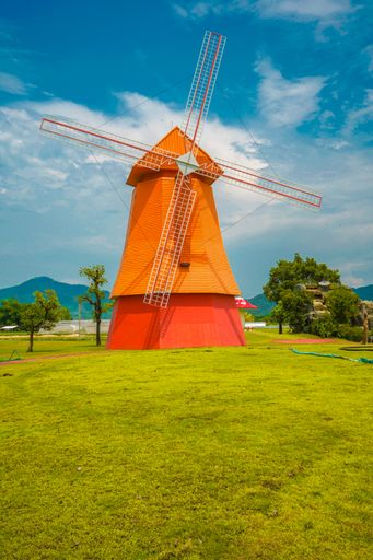 A vertical shot of a colorful windmill in a rural area on cloudy sky background