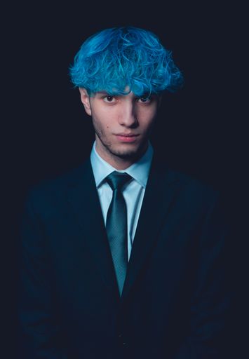 A vertical shot of cool Spanish man entrepreneur with blue hair isolated on black background
