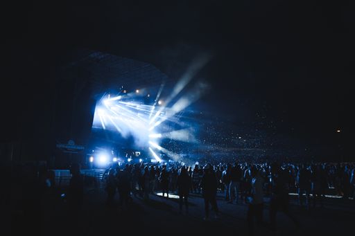 A big crowd enjoying a concert from a blue illuminated stage