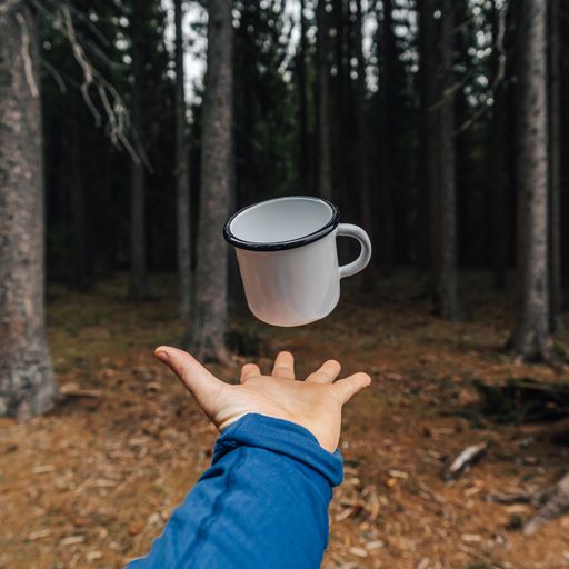 White enamel cup flying or levitating above a hand. White outdoor or camping cup photo. Metal camping mug.