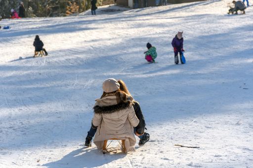 A back shot of two girls riding a wooden sled down sledding hill on a sunny winter day
