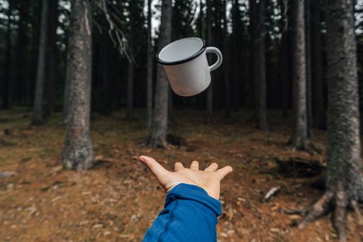 White enamel cup flying or levitating above a hand. White outdoor or camping cup photo. Metal camping mug.