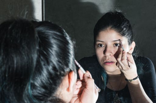 A view of a beautiful Latina girl looking at the mirror and putting makeup for herself