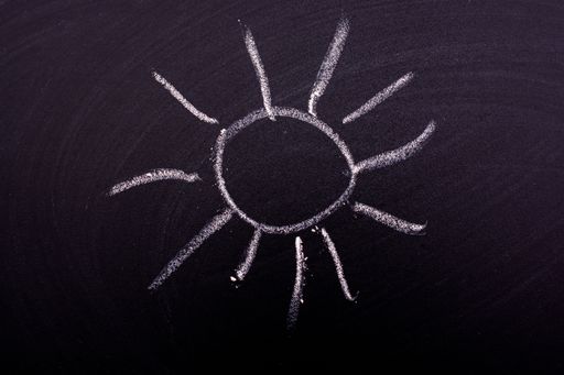 A closeup shot of a sun drawn on a blackboard with  chalk