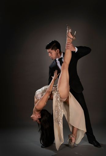 A tango couple of Hispanic woman and Asian man dancing with studio black background