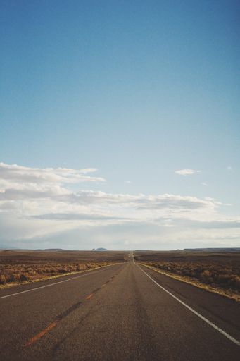 A vertical shot of an empty road in the middle of a desert under a beautiful blue sky