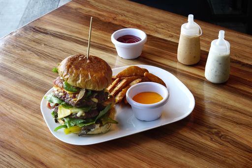 A cheeseburger with french fries and a sauce in a white plate on a wooden table