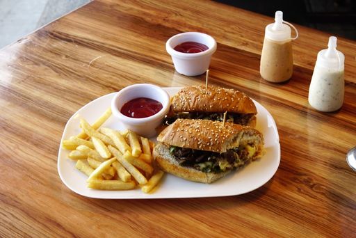 A cheeseburger with french fries and a sauce in a white plate on a wooden table