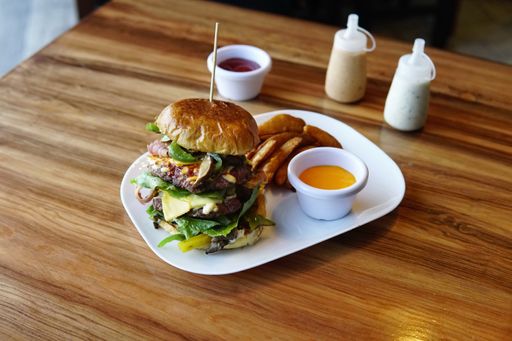 A cheeseburger with french fries and a sauce in a white plate on a wooden table