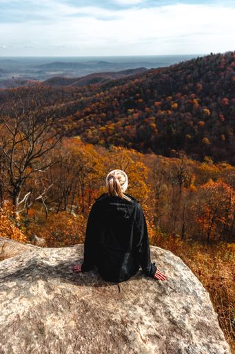 A back view of a woman sitting on the stone and admiring the mountains with bright orange trees