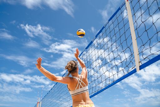 A low angle shot of a volleyball player jumping against the net to hit the ball in bright sunlight against the blue cloudy sky in Melbourne, Australia