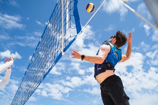 A low angle shot of a volleyball player jumping against the net to hit the ball in bright sunlight against the blue cloudy sky in Melbourne, Australia