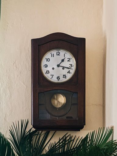 A vertical closeup shot of a vintage brown clock hanging on the wall