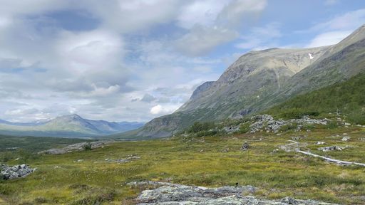 A beautiful landscape of a green meadow against mountains and cloudy sky on a sunny day