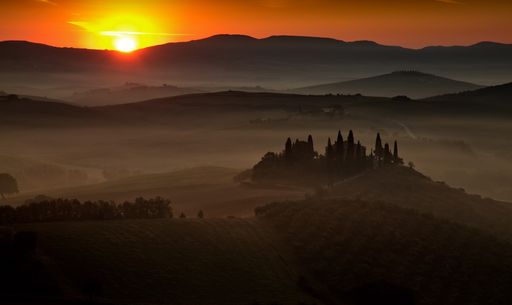 A landscape of hill silhouettes covered in the fog during a beautiful sunset in Tuscany, Italy