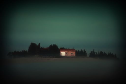 A shallow focus shot of a rural house with trees around  against blue sky at evening in Tuscany, Italy
