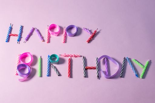 A Happy Birthday text made of candles and ribbons isolated on pink background
